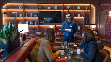 A restaurant with a modern interior, featuring red cushioned seating, a central table with a waiter, and a TV mounted on the wall.