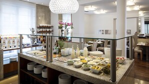 Zona de buffet amb diversos plats i begudes, una barana de vidre i un lampadari.