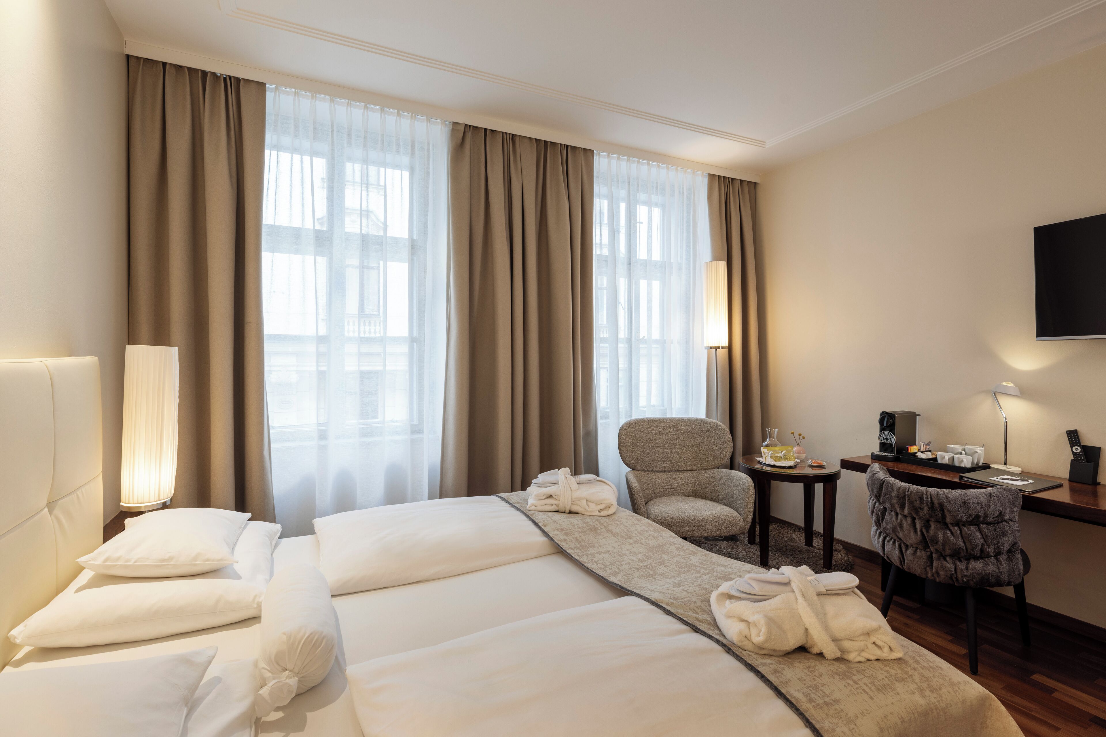 A hotel room with two beds, a desk, a chair, and a TV.