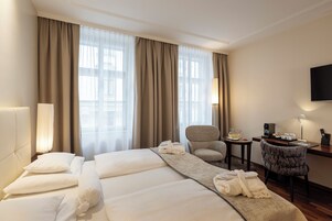 Quarto de hotel com duas camas, uma escrivaninha, uma cadeira e uma televisão.