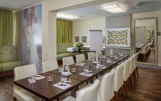 Uma sala de conferências com uma mesa comprida, cadeiras brancas e um quadro branco com fotos.