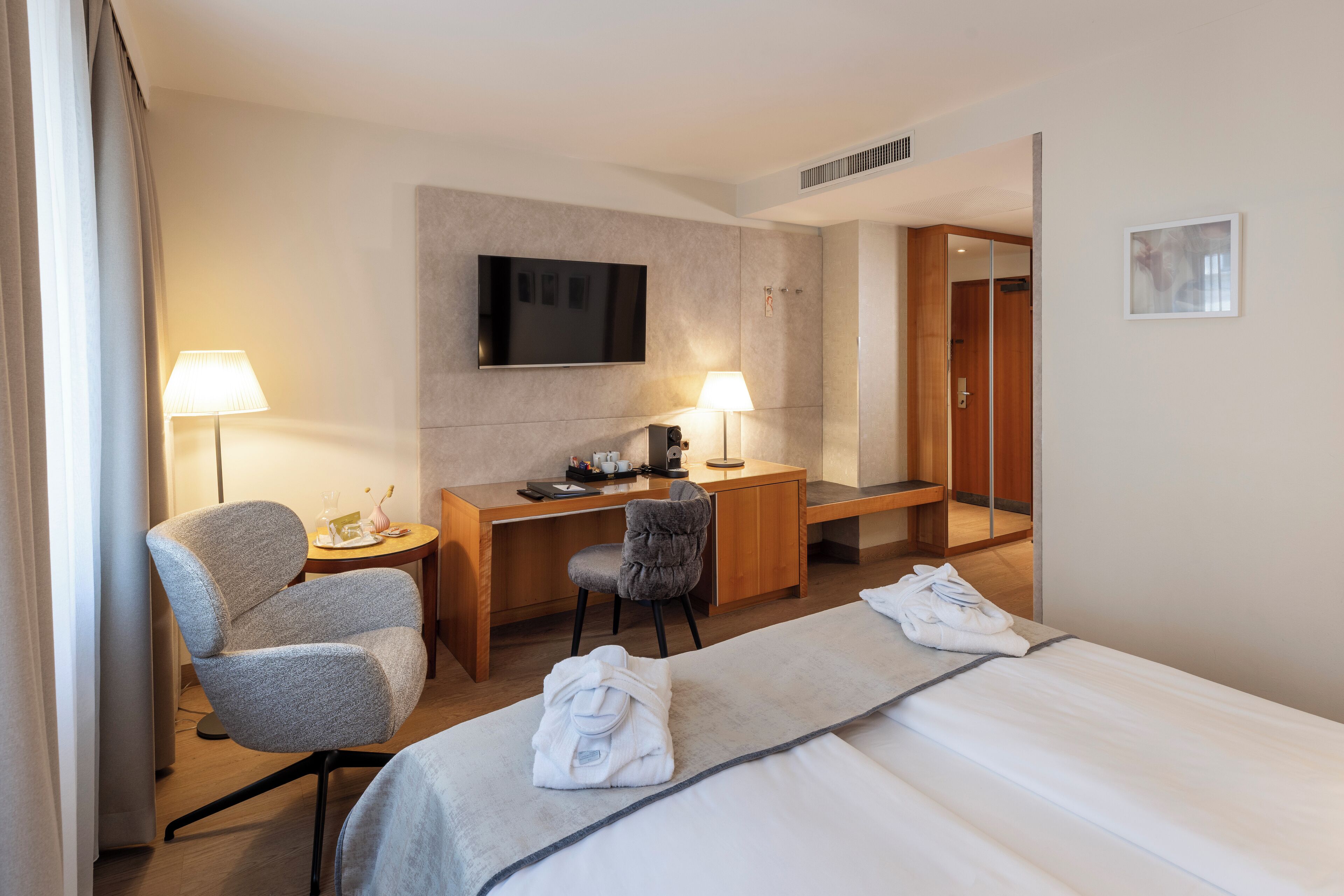 Une chambre d’hôtel comprenant un lit, deux chaises, un bureau, une télévision et deux lampes.