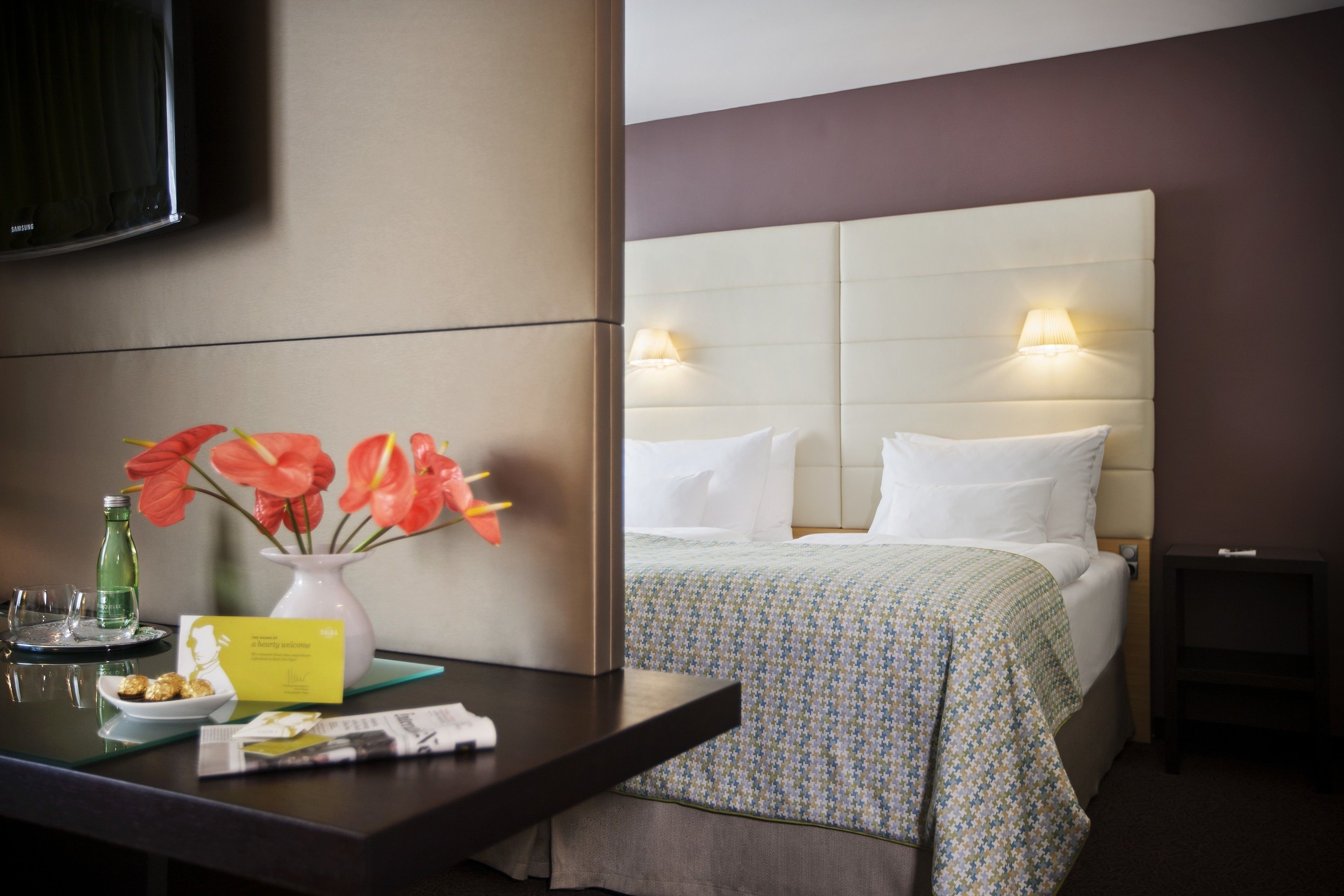 A hotel room with a bed, bedside table, lamp, and a flat-screen TV.