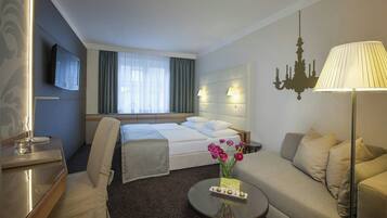 Una camera d'hotel con un letto, un divano, un tavolino, una televisione e un lampadario.
