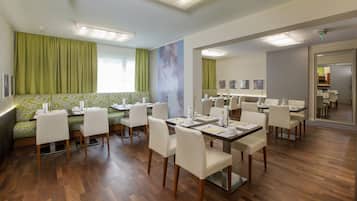 Un comedor de hotel con cortinas verdes, un sofá y varias mesas de comedor con sillas.