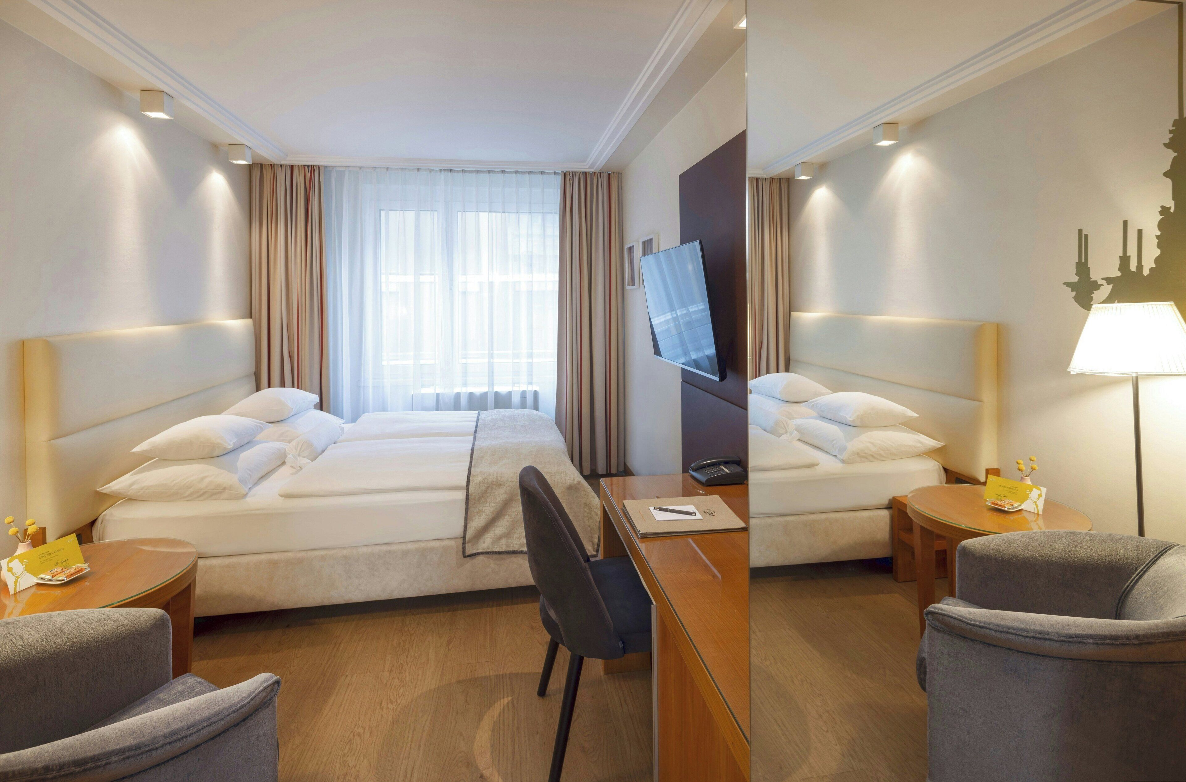 A hotel room with a bed, a desk, a chair, a TV, and a lamp.