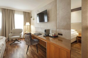 Quarto de hotel com cama, escrivaninha, cadeira, televisão, luminária e cafeteira.