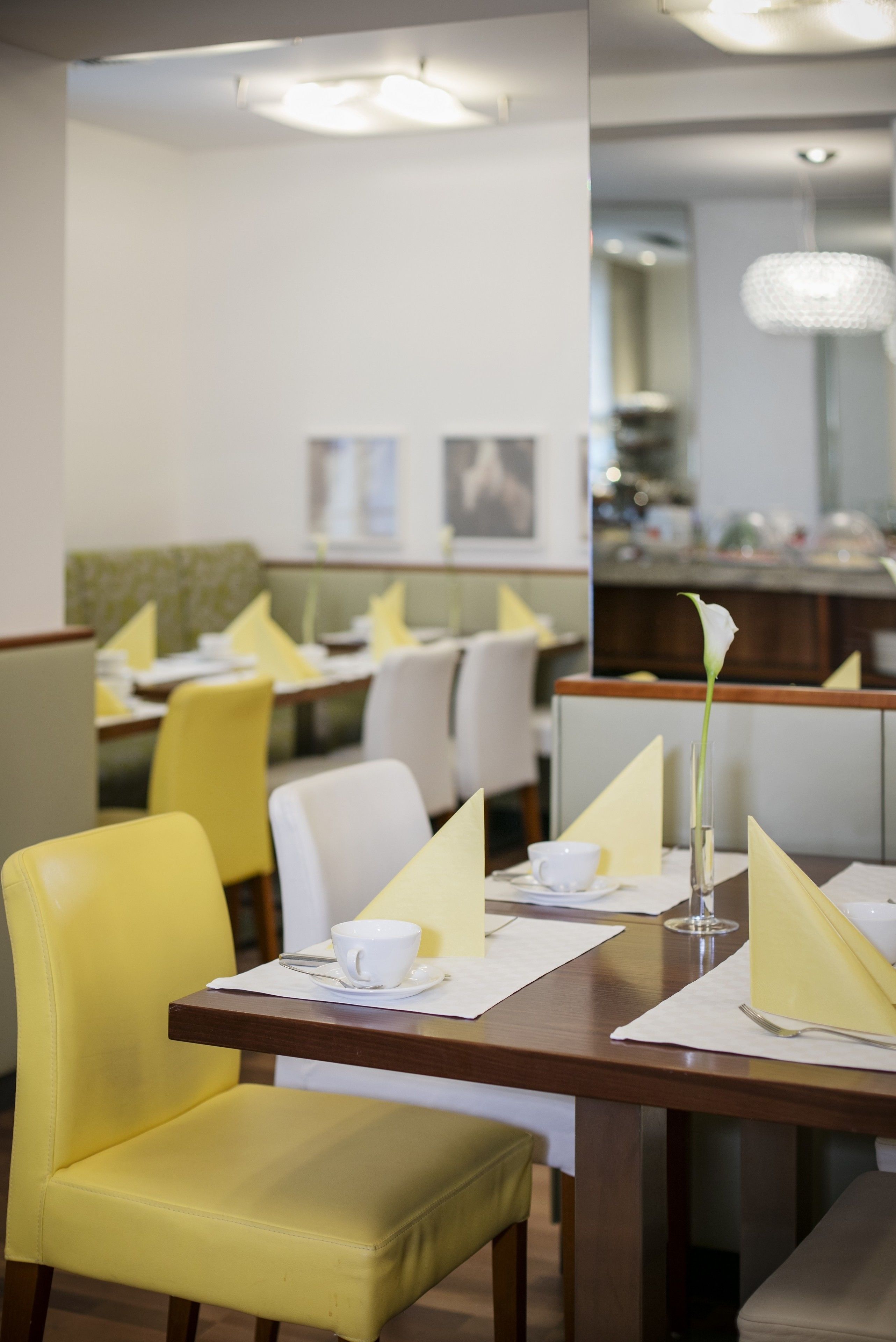 A dining area with yellow chairs, white table settings, and a vase with a white flower.