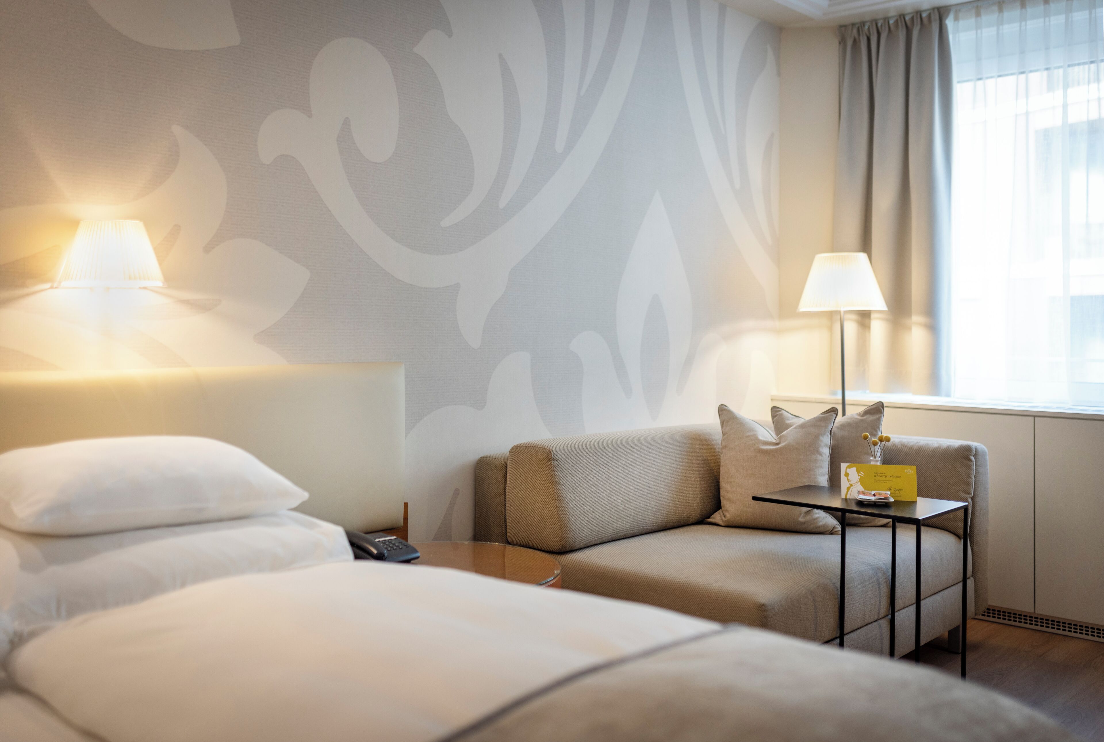 Een hotelkamer met een bed, een bank, een klein tafeltje, twee lampen en een raam met gordijnen.