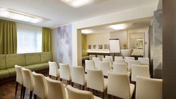Un salón de conferencias con un sofá verde, sillas blancas, una pizarra y un espejo.