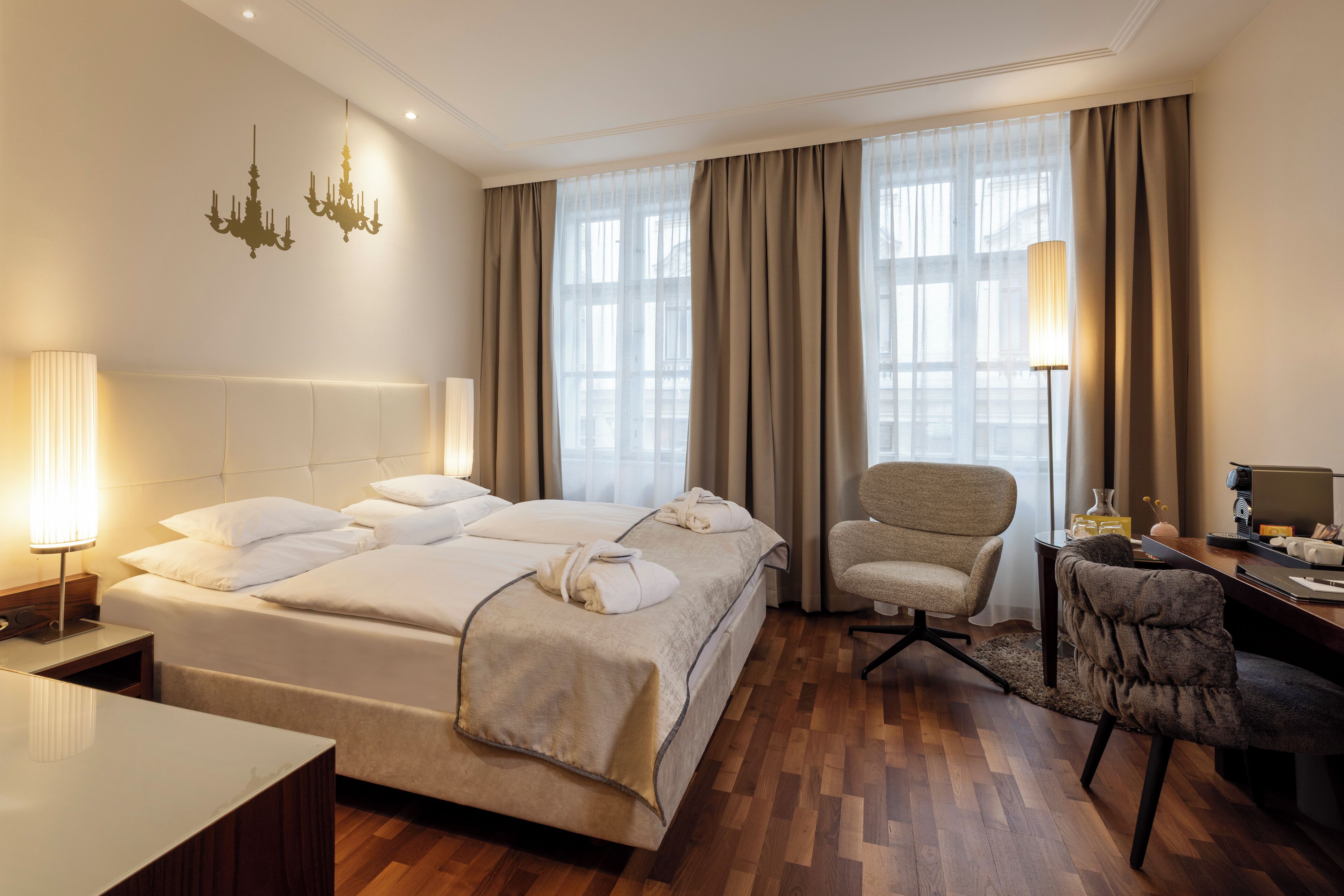 Una habitación de hotel con cama, escritorio, silla, lámpara y candelabro.