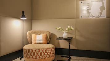 Una habitación moderna con un pouf redondo, una mesita con un jarrón de flores y un cartel en la pared que indica los números de las habitaciones y una sala de seminarios.