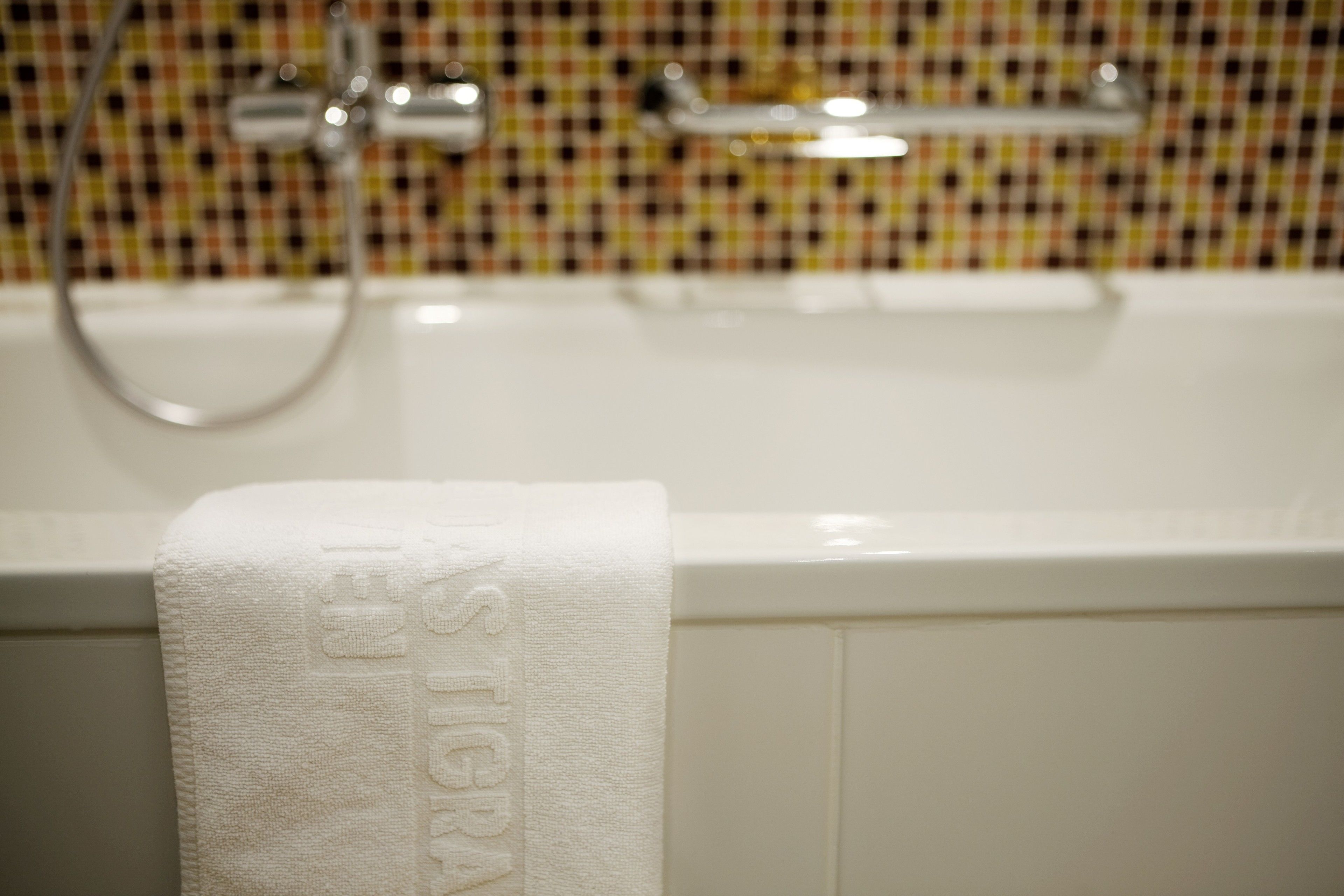 A white bathtub with a towel hanging on the side, a showerhead, and a tiled wall with a checkered pattern.