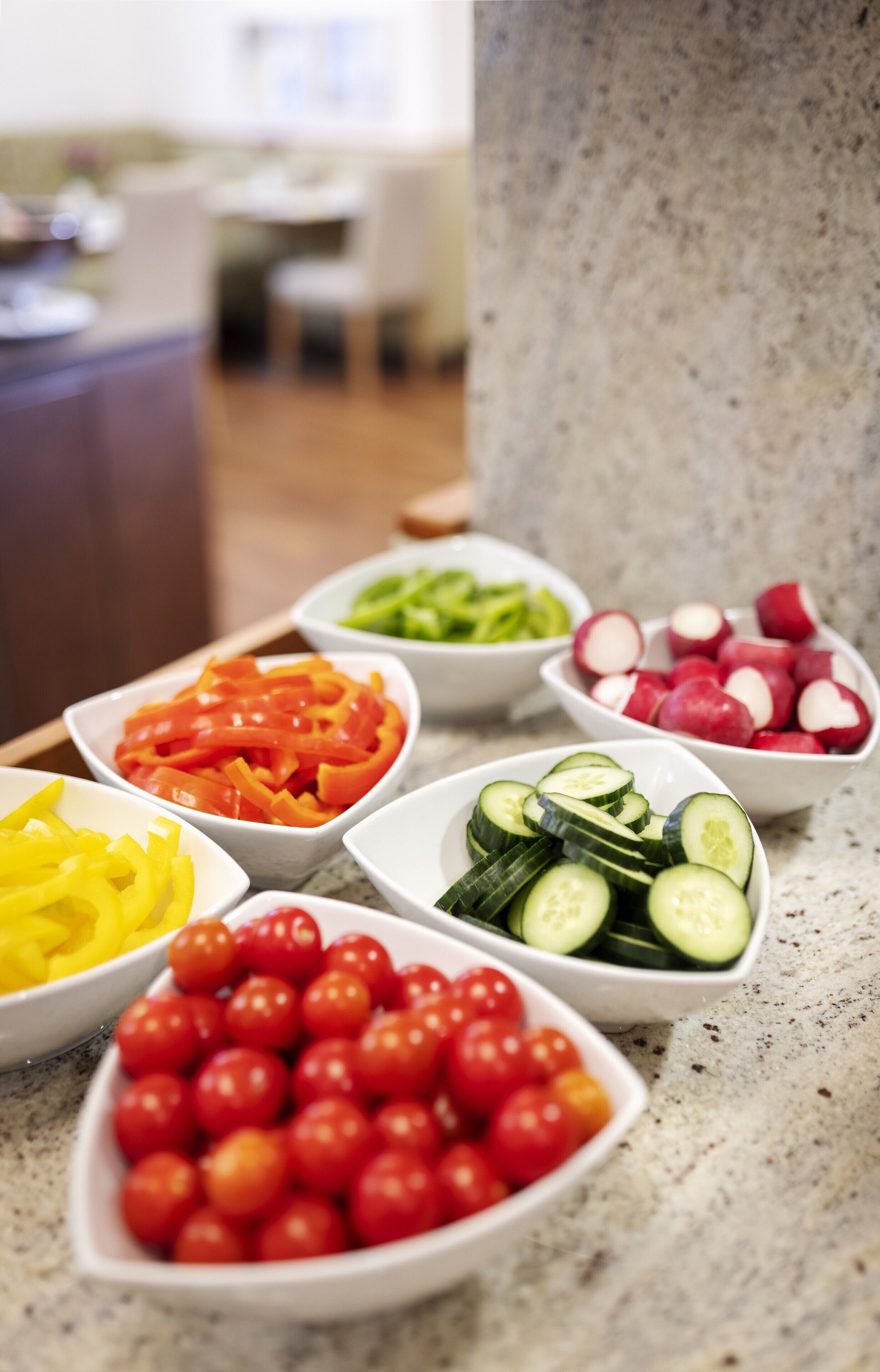 A kitchen counter with various bowls of sliced vegetables.