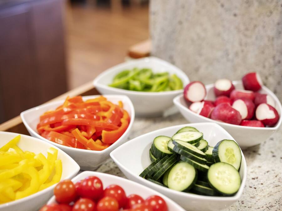 A kitchen counter with various bowls of sliced vegetables.