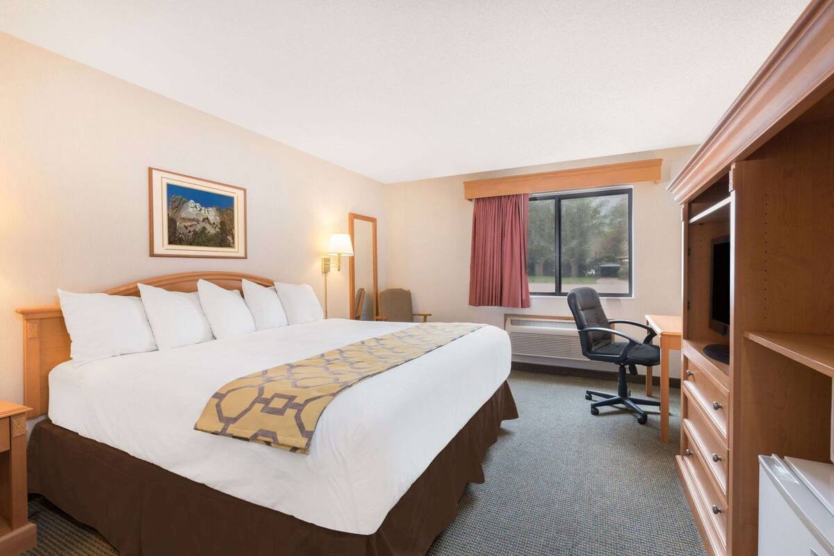 A hotel room with a large bed, a desk, a chair, a television, and a window with curtains.