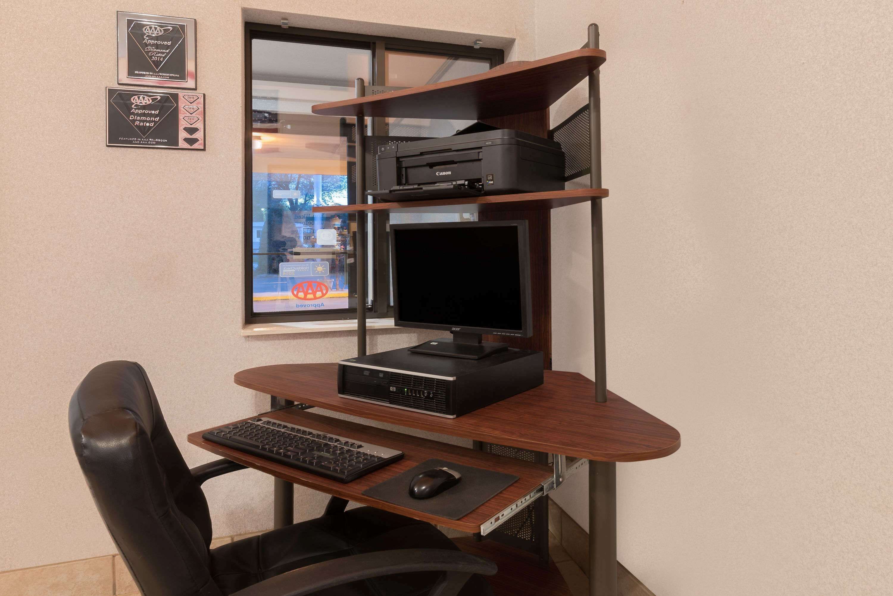 Um espaço de escritório em casa com mesa, cadeira, computador, monitor, impressora e estantes.