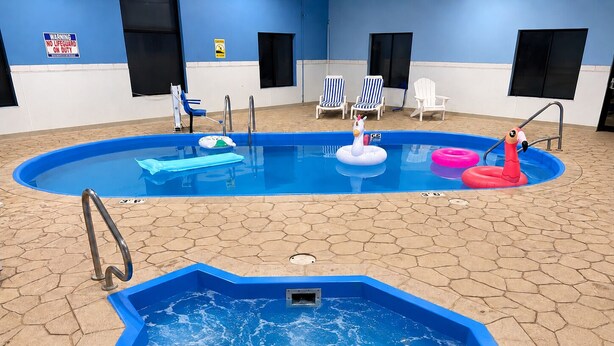 An indoor swimming pool with a hot tub, lounge chairs, and inflatable toys.