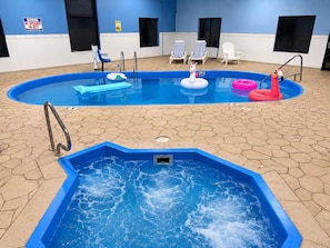 An indoor swimming pool with a hot tub, lounge chairs, and inflatable toys.
