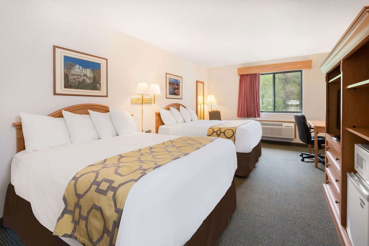 A hotel room with two beds, a desk, a chair, a TV, and a window with curtains.