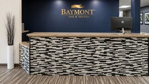 Un mostrador de recepción con el logotipo de Baymont Inn & Suites, una computadora de escritorio y una pared decorativa con un patrón geométrico.