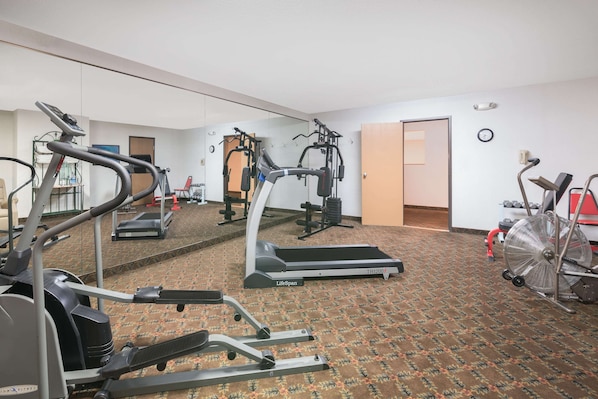 Ein Fitnessraum mit Laufbändern, Crosstrainern und einer Spiegelwand.