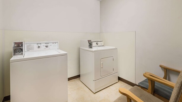A laundry room with two white washers and dryers, a wooden bench, and a tiled floor. - Baymont by Wyndham Hot Springs (Hot Springs)