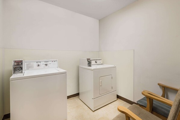 A laundry room with two white washers and dryers, a wooden bench, and a tiled floor. - Baymont by Wyndham Hot Springs (Hot Springs)
