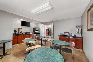 A room with a kitchenette, a flat-screen TV, and a dining area with tables and chairs.