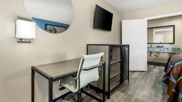 A hotel room with a desk, chair, TV, and a bathroom with a mirror and sink.
