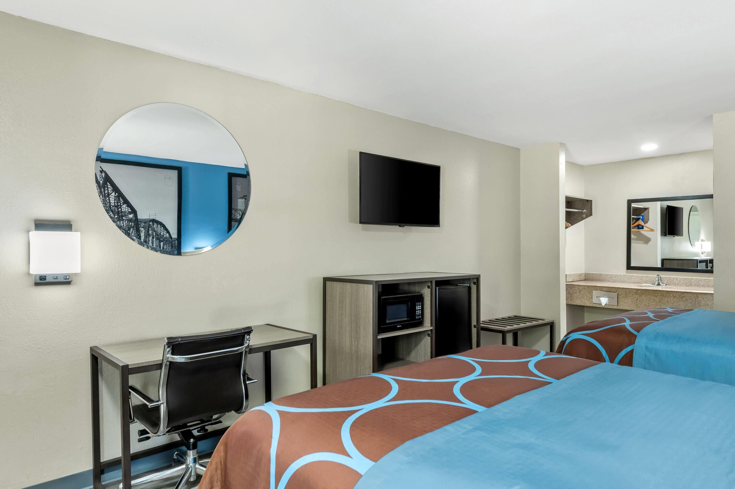 A hotel room with two beds, a TV, a microwave, a small table, a chair, and a mirror.