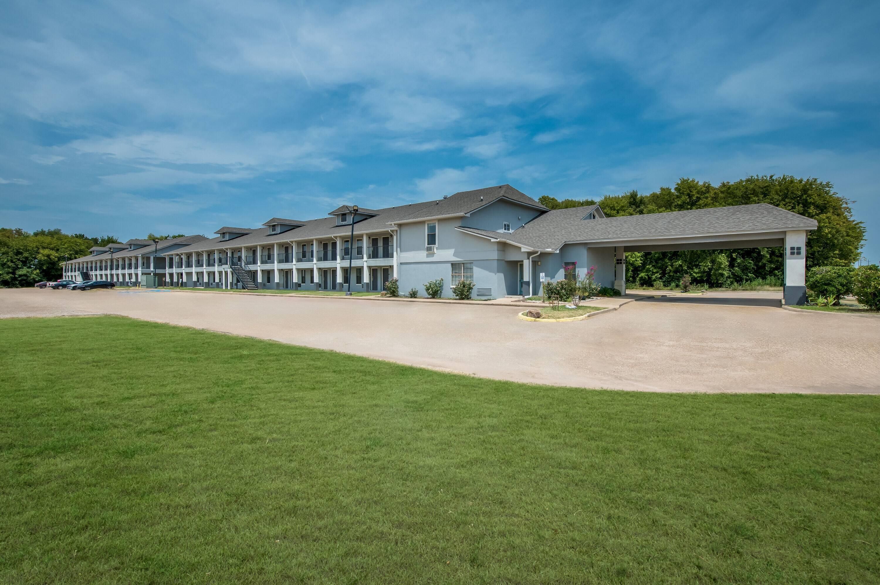 A multi-story motel with a covered parking area and a well-maintained lawn.