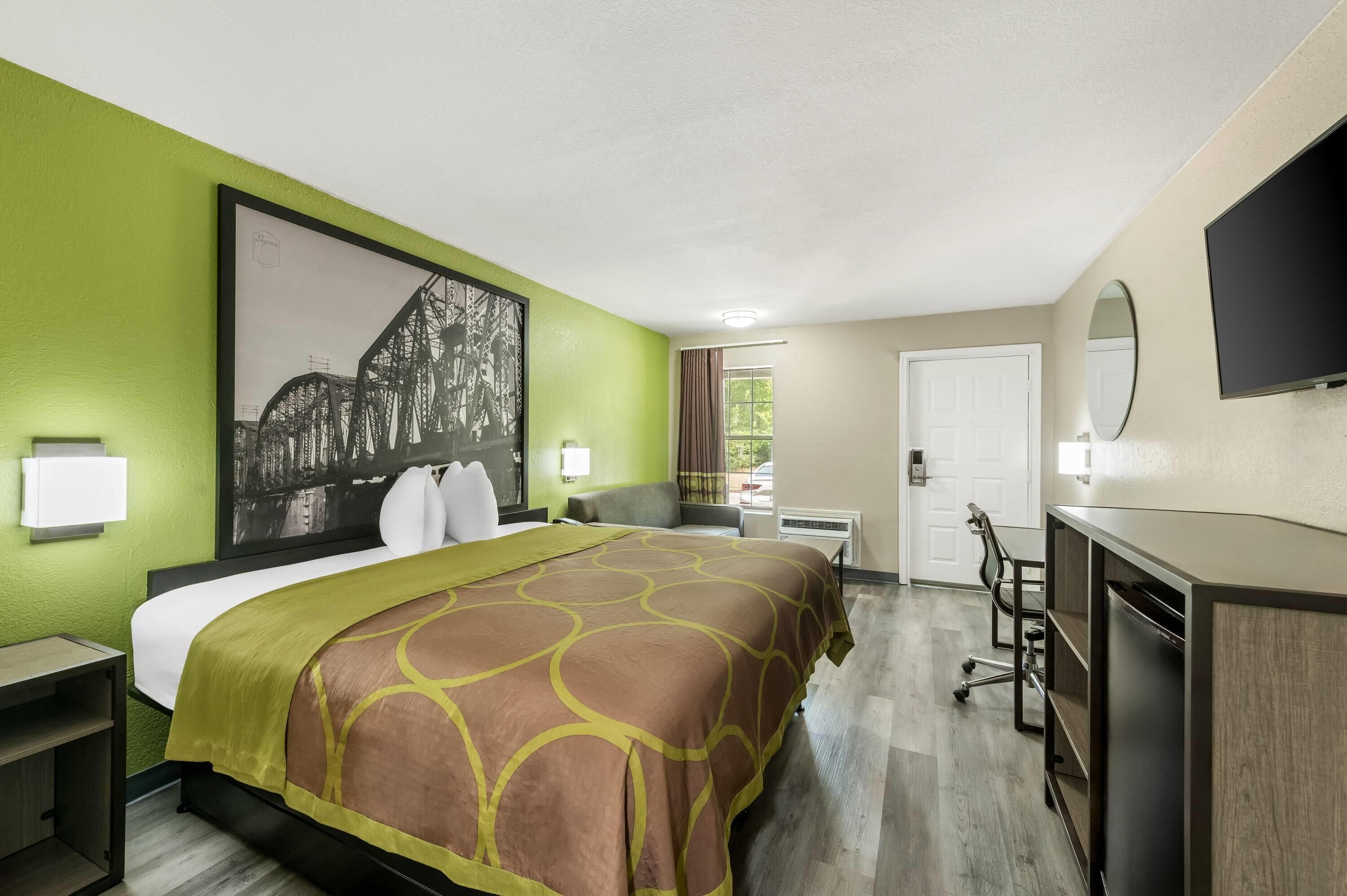 A hotel room with a bed, a desk, a chair, a television, and a window with curtains.