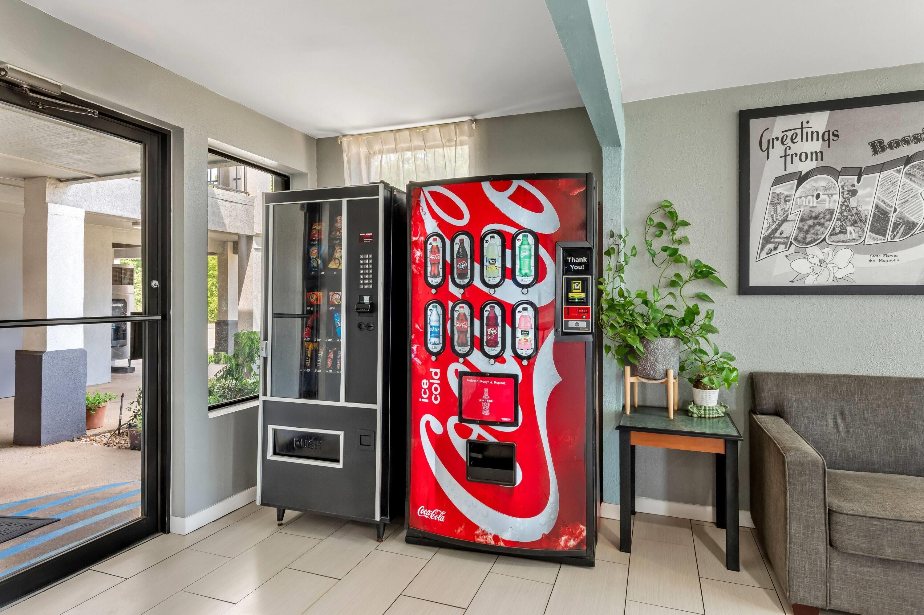 Ein Getränkeautomat mit Coca-Cola-Logo, einem Glastür-Eingang und einem gerahmten Bild an der Wand.