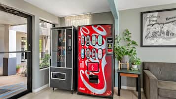 Ein Getränkeautomat mit Coca-Cola-Logo, einem Glastür-Eingang und einem gerahmten Bild an der Wand.