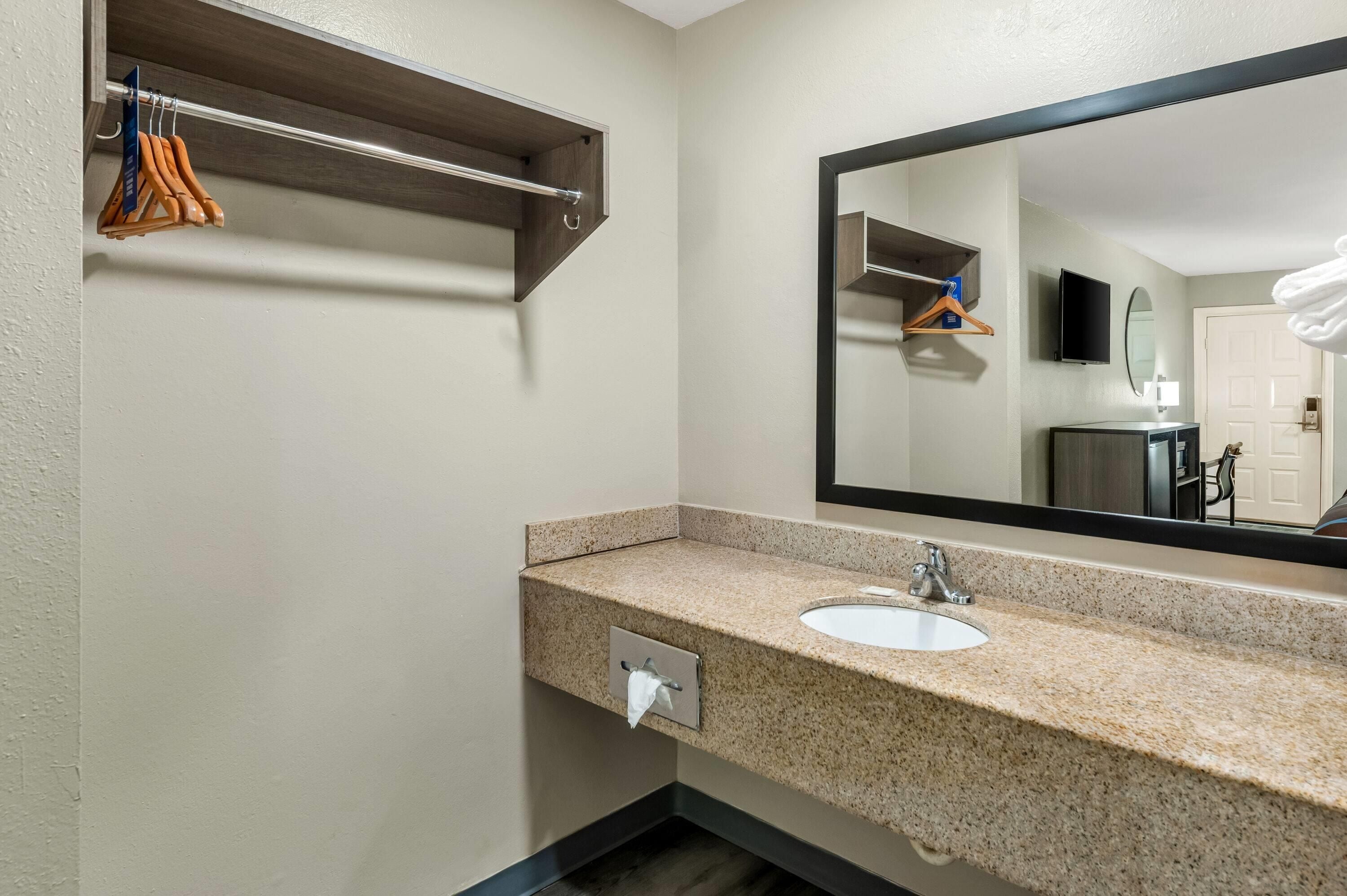 A hotel bathroom with a granite countertop, a sink, a mirror, and a towel rack.