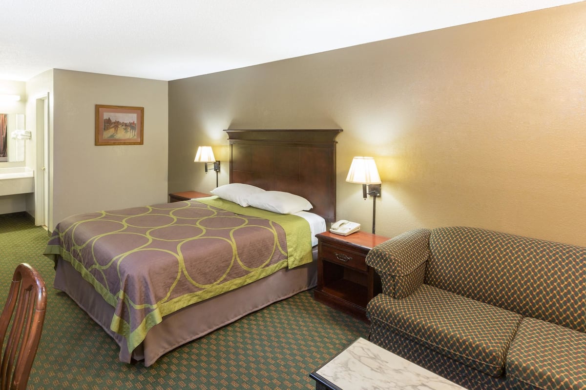 A hotel room with a bed, a nightstand with a lamp, a sofa, and a chair.
