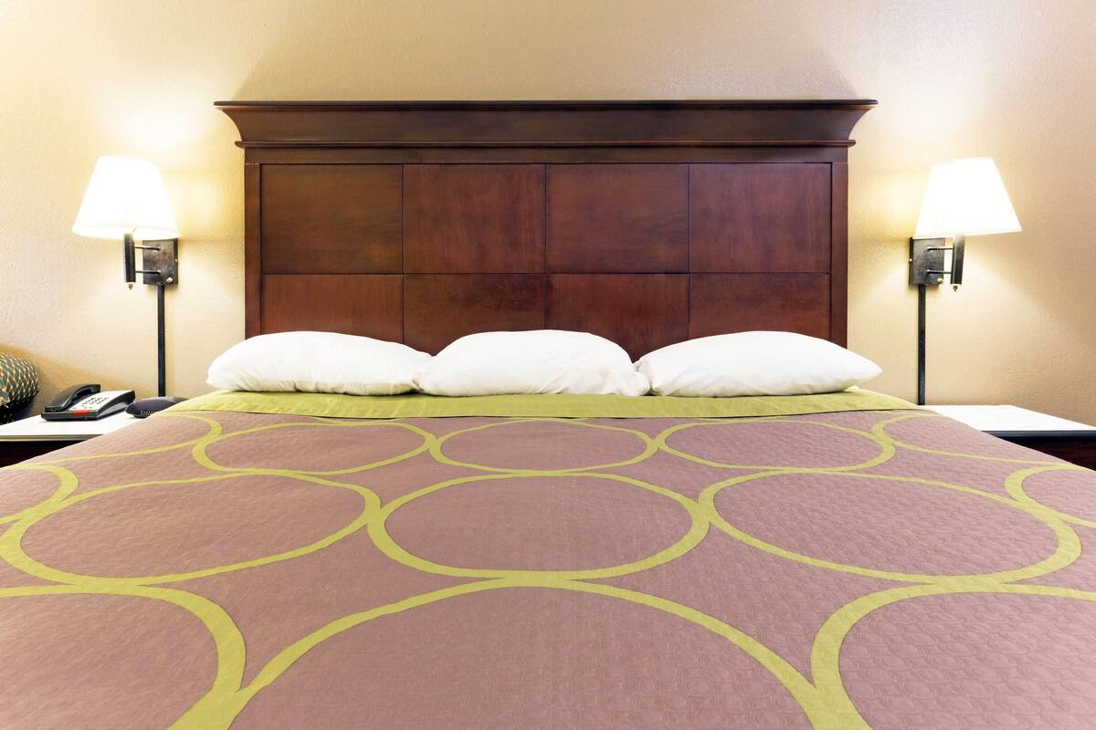 A hotel room with a large bed, two bedside lamps, a telephone, and a green and pink patterned bedspread.