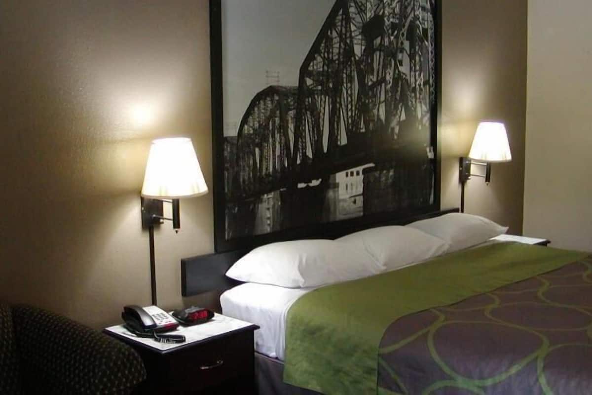 A hotel room with a bed, two bedside lamps, a telephone, and a chair.