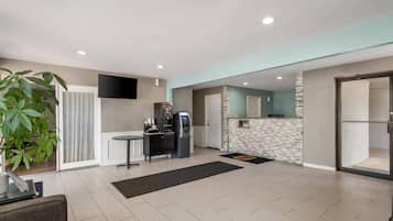 A modern living room with a flat-screen TV, a coffee machine, and a dining area with a table and chairs.