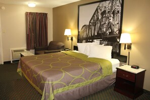 A hotel room with a bed, a chair, a nightstand, a lamp, a wall-mounted heater, and a large framed picture of a bridge. - Super 8 by Wyndham Bossier City/Shreveport Area (Bossier City)