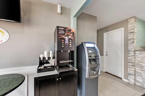 Máquina de café com o logo Nescafe, um caixa eletrônico e uma televisão fixada na parede.