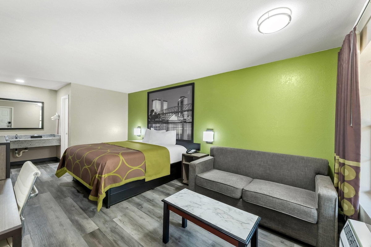 Una camera d'hotel con un letto, un divano, un tavolino, una scrivania con un telefono e un bagno con uno specchio e un lavandino.