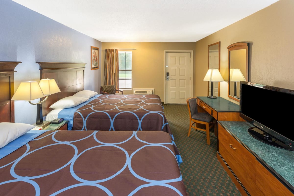 A hotel room with two beds, a desk with a television, a chair, and a door.