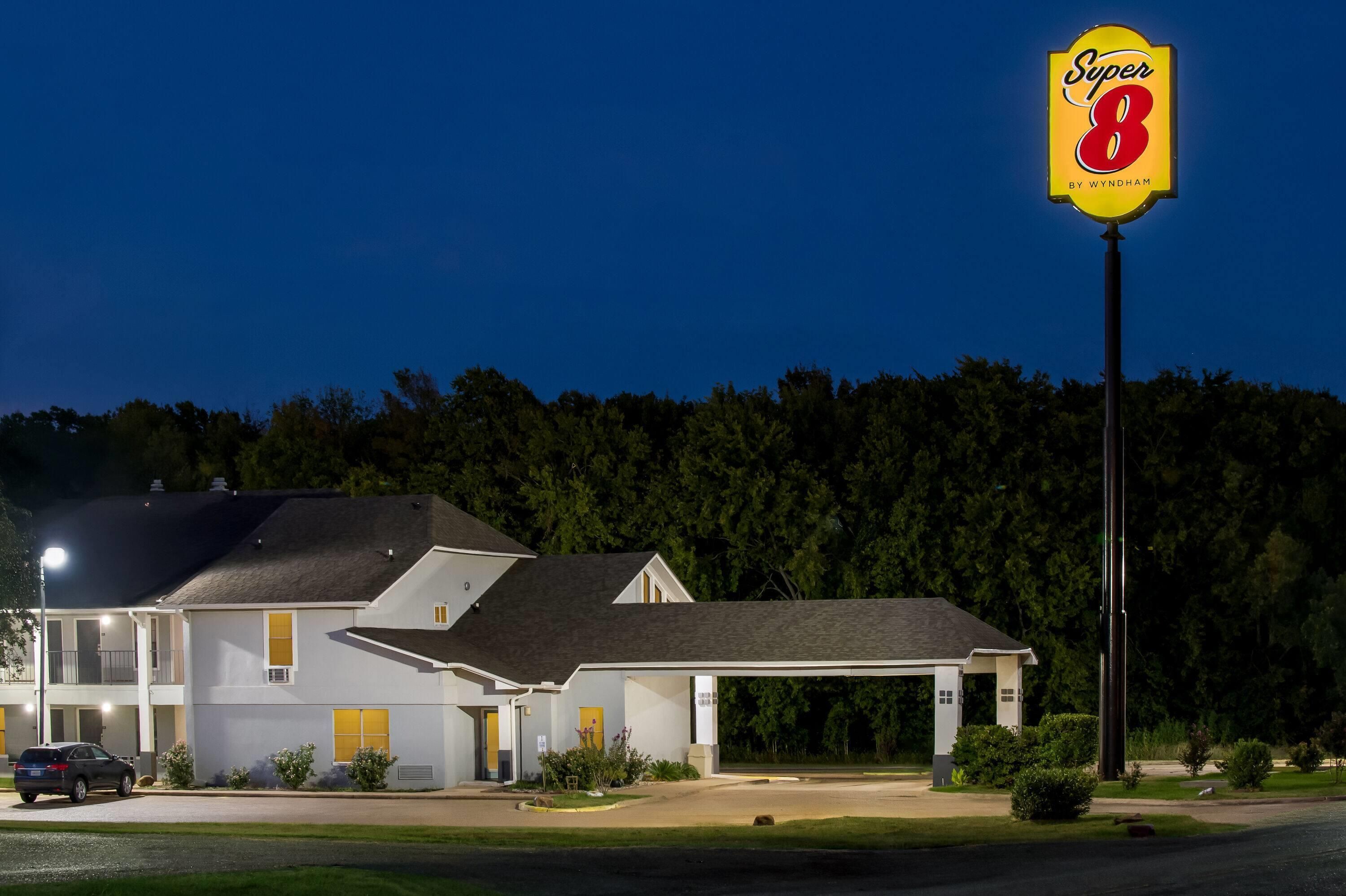 Ein Motel mit einem gut sichtbaren 'Super 8'-Schild, ein eingeschossiges Gebäude mit flachem Dach und einem Parkplatz davor.