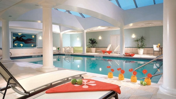 An indoor swimming pool with a skylight, lounge chairs, and decorative flowers. - Westminster Hotel (Livingston)