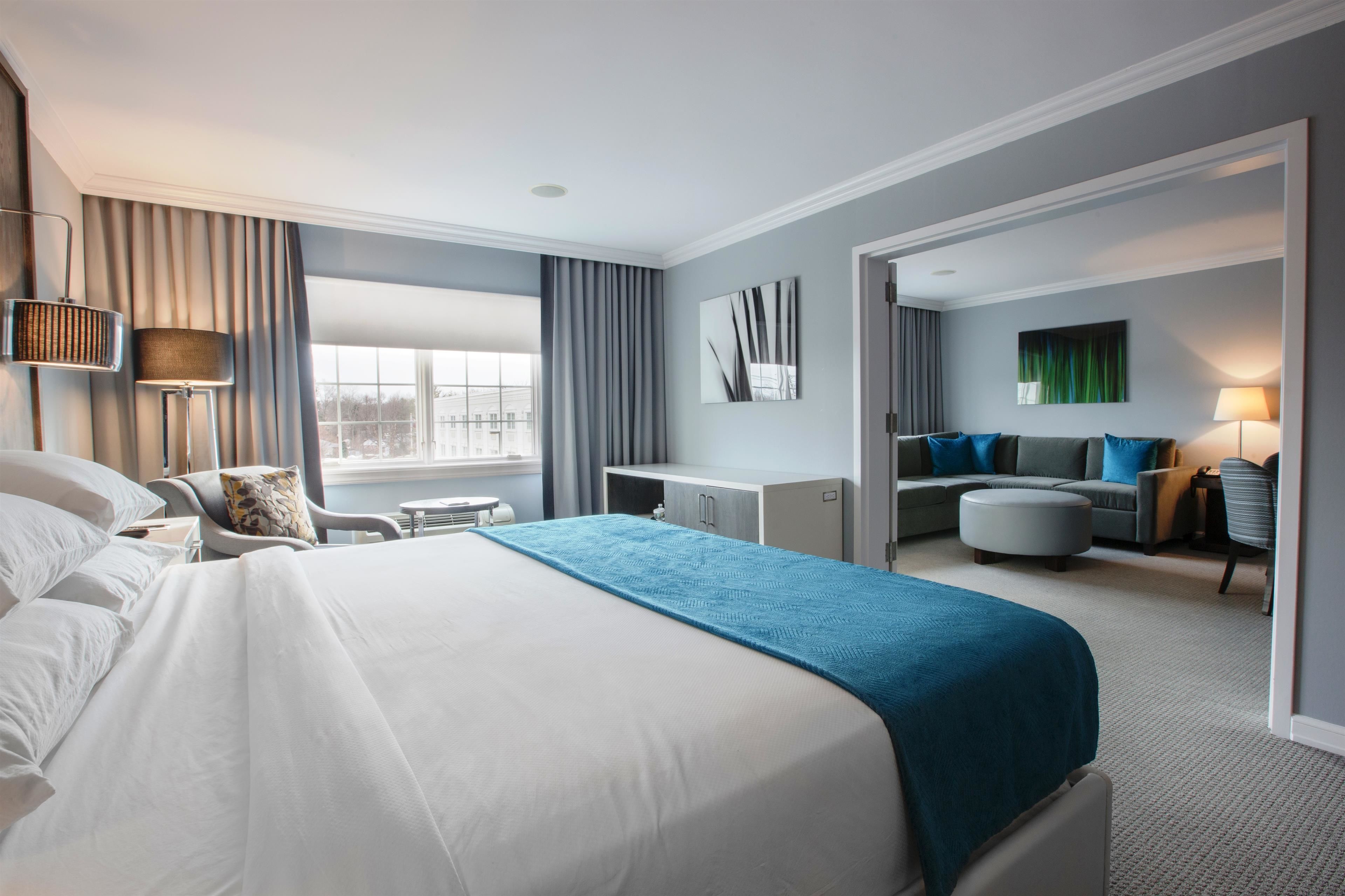 A modern hotel room with a large bed, a desk, a sofa, and a view of the city.