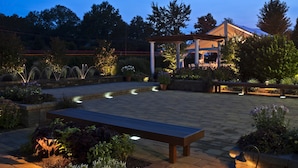 An outdoor patio area with a wooden bench, potted plants, and a pergola structure. - Westminster Hotel (Livingston)