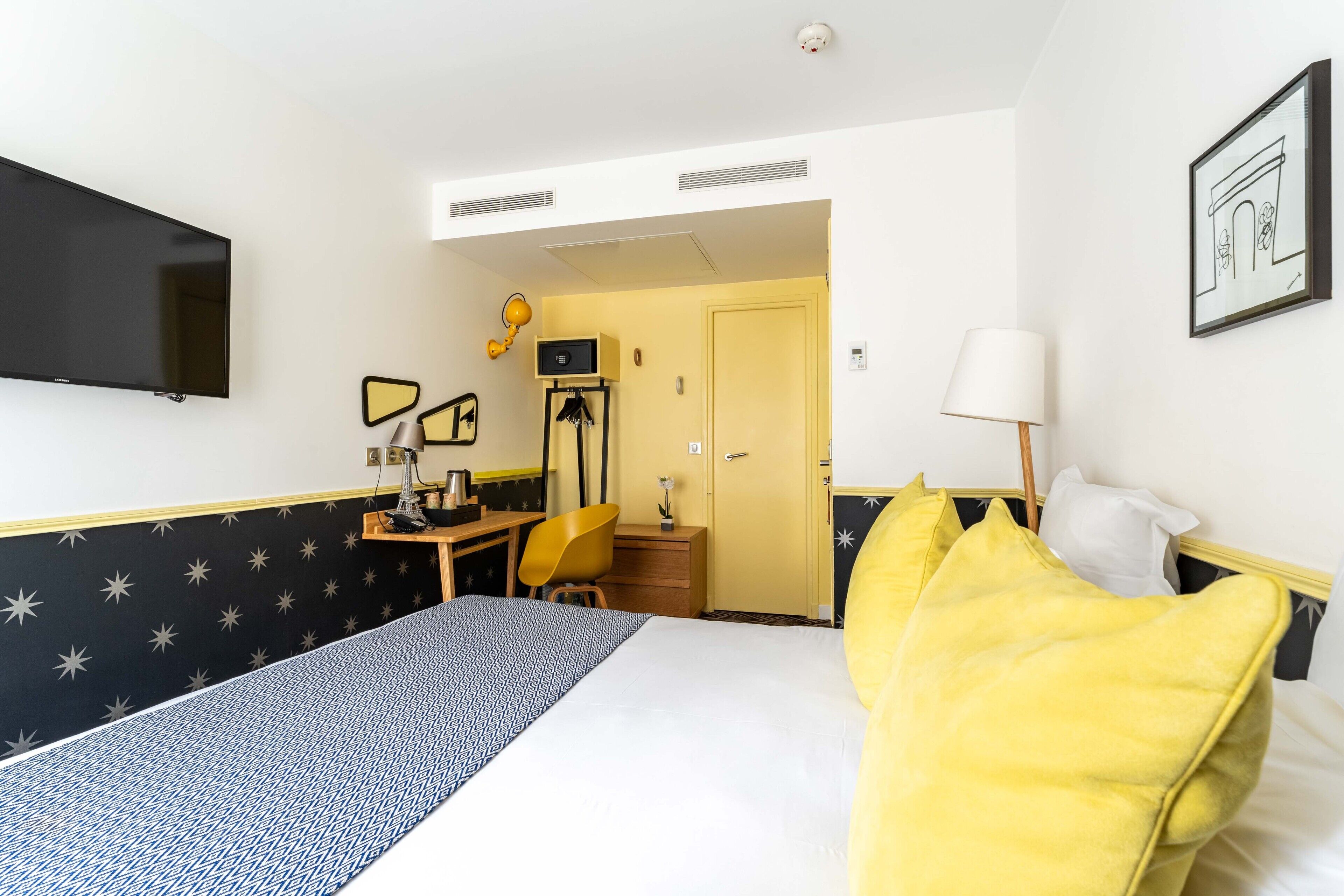 Quarto de hotel com cama, escrivaninha, cadeira, televisão e porta para o banheiro.