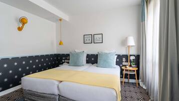 A hotel room with a bed, a bedside table with a lamp, a small table with a plant, and star-patterned walls.